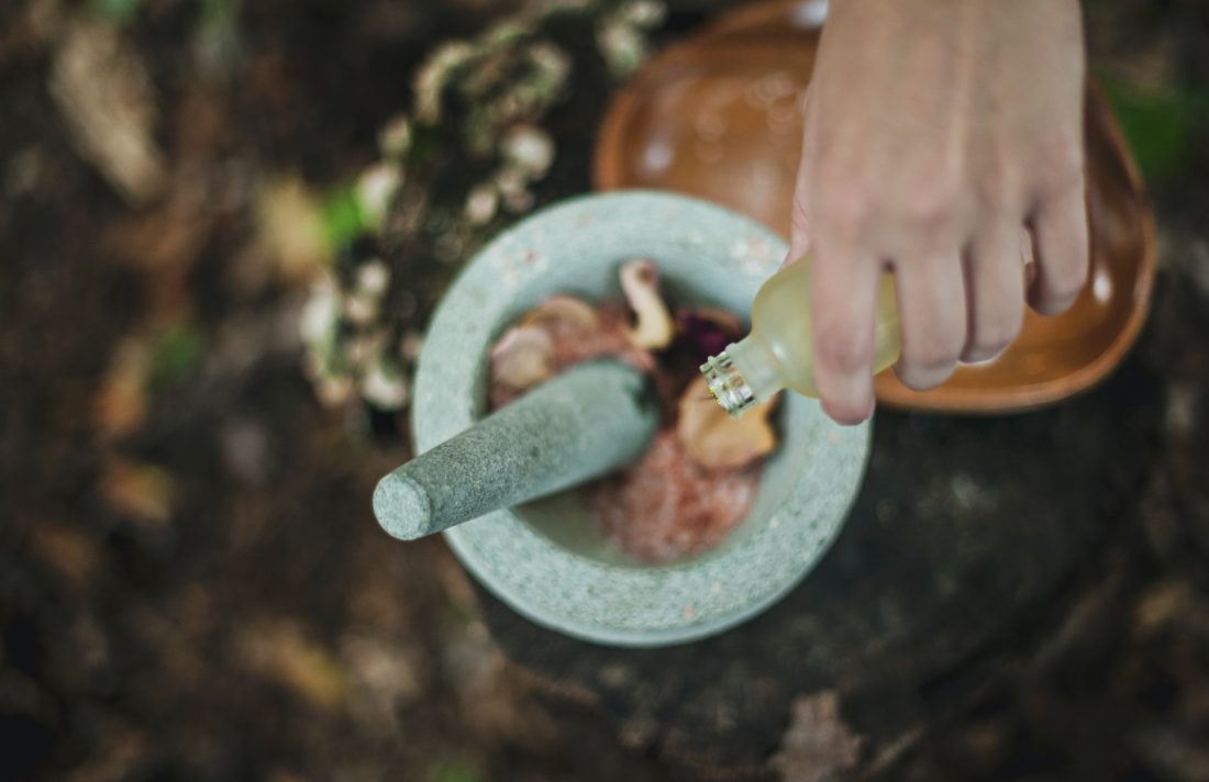 woman's hand pouring essential oils into a mortar and pestle filled with flowers