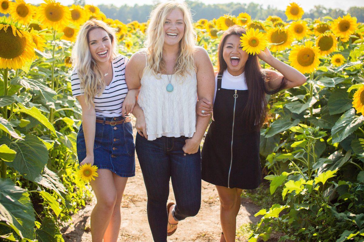 three woman standing in sunflower field