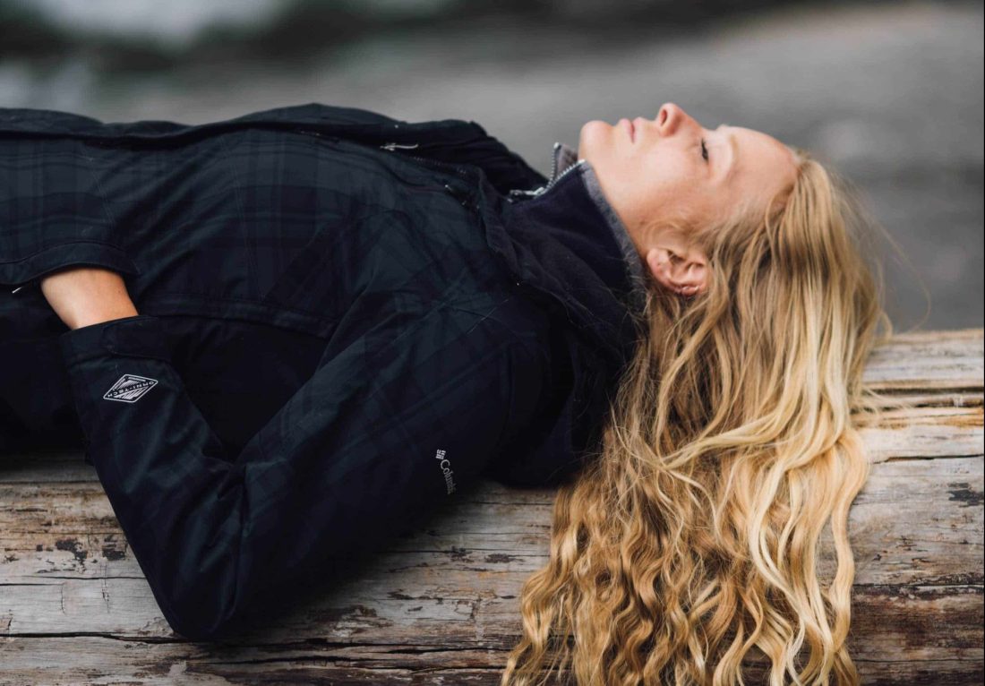 woman with eyes closed laying on log outside