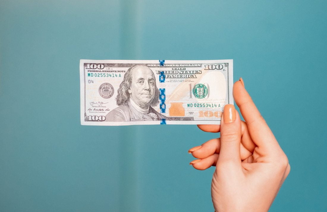 woman's hand holding 100 dollar bill