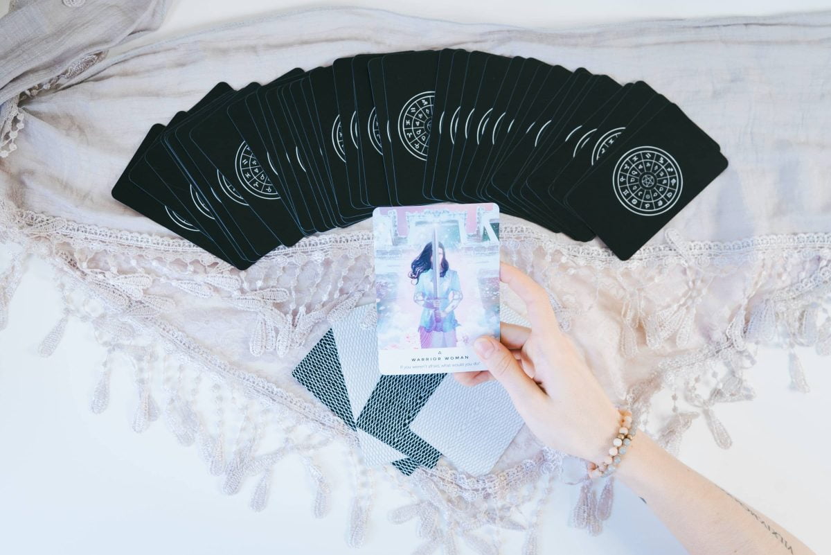 woman holding one tarot card over a deck of tarot cards on a pink cloth