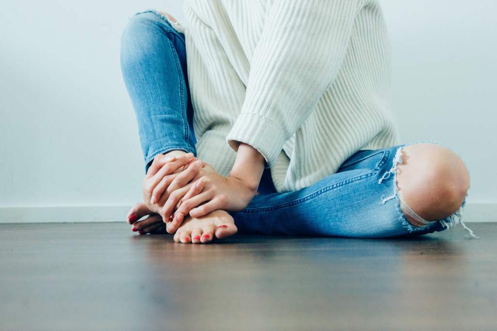 woman in white sweater and jeans touching her bare feet