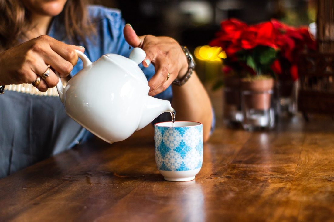 woman pouring moon water from a white tea pot into a blue and white mug