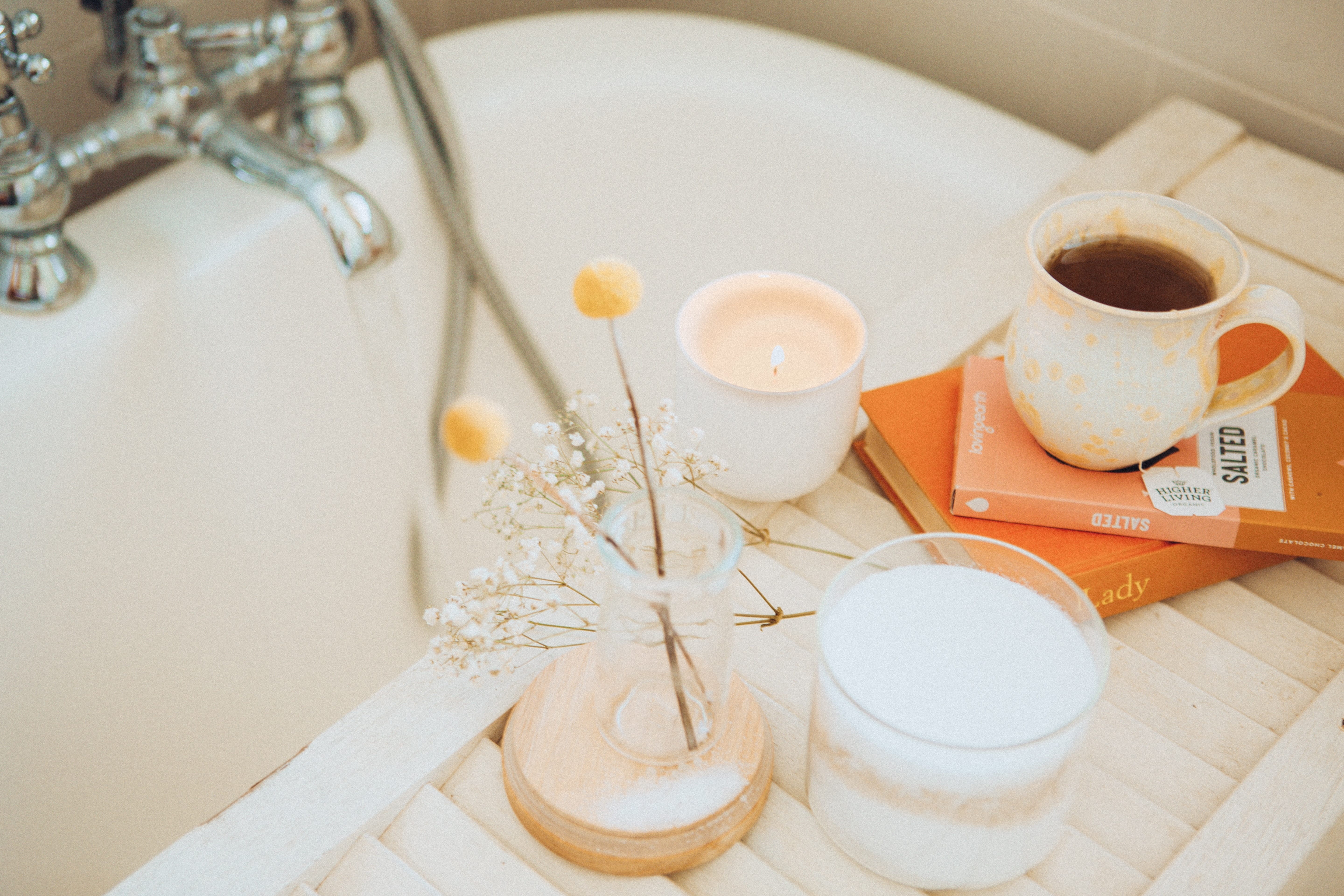 bath tub with tray holding flowers, candles, books, and tea