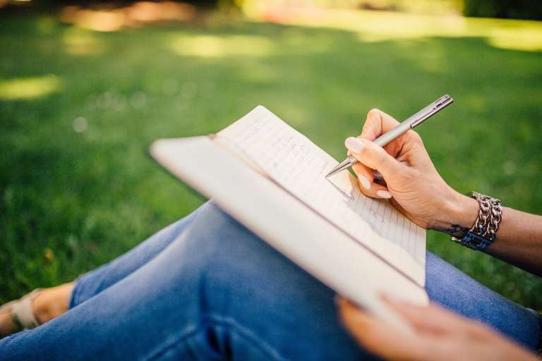 woman in jeans outdoors writing in notebook