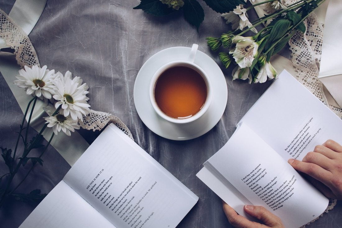 open poetry book on a table with a cup of tea and flowers
