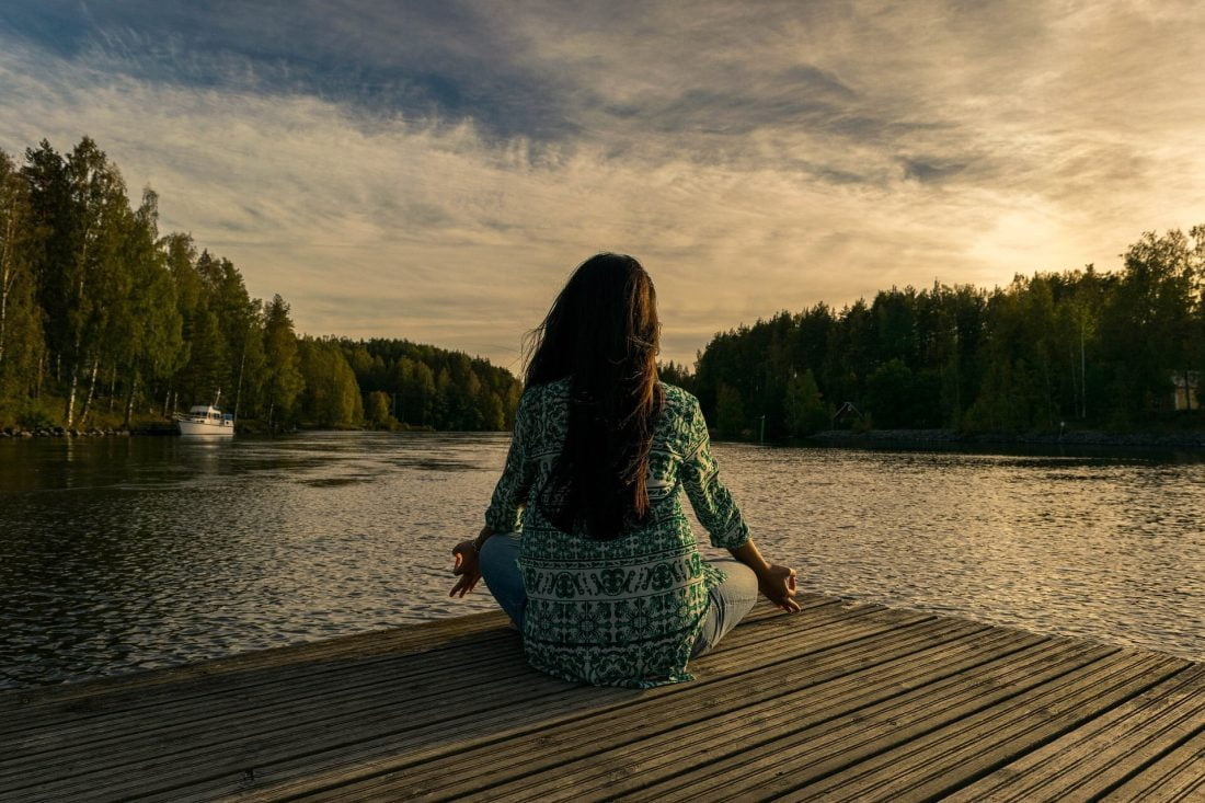 woman meditating on a dock at sunset
