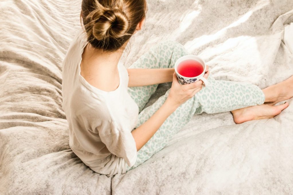 woman sitting on bed drinking a cup of pink tea