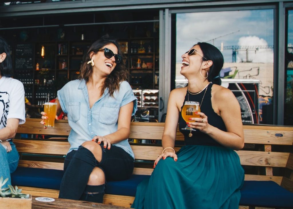 two women laughing and drinking outside