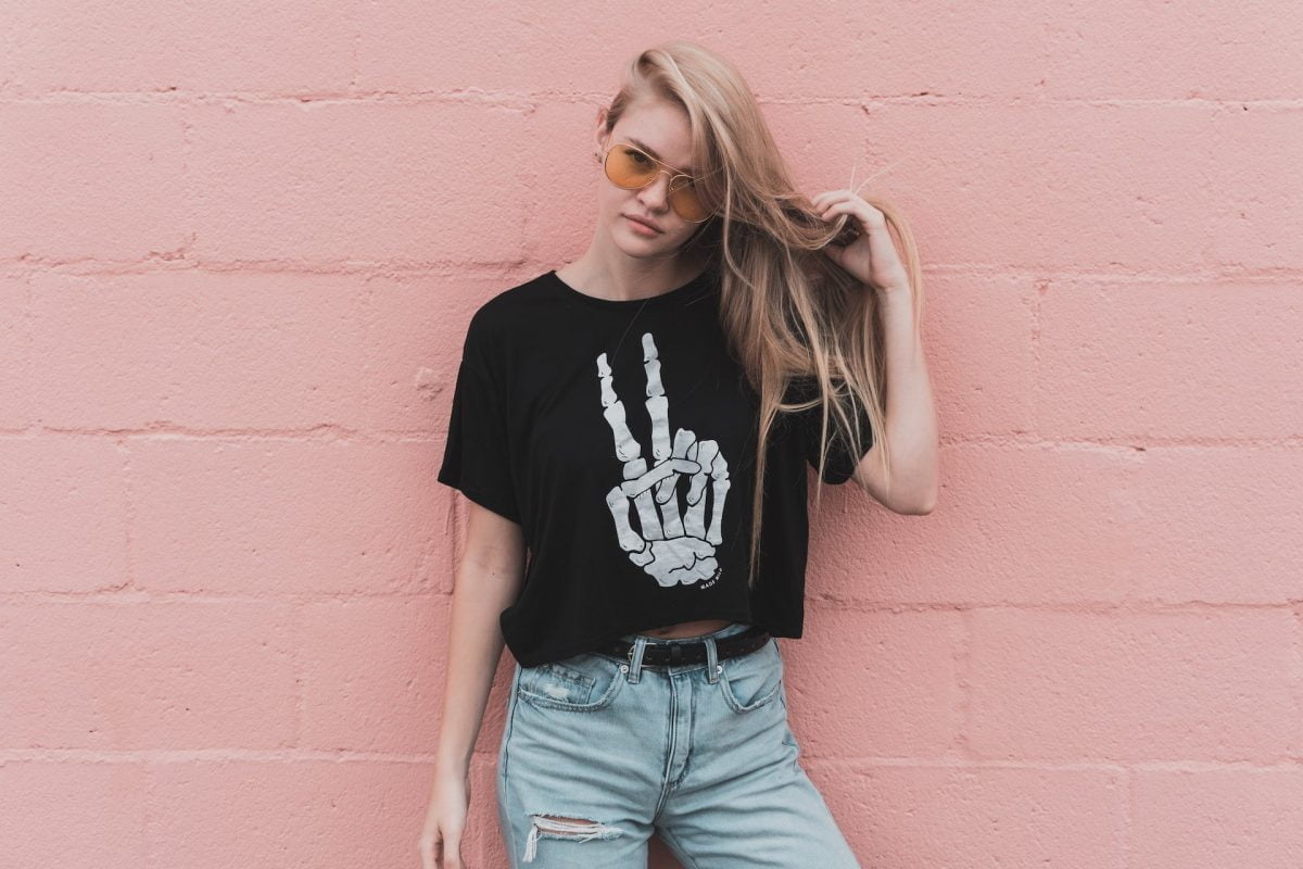 woman in black tee and sunglasses against a pink wall