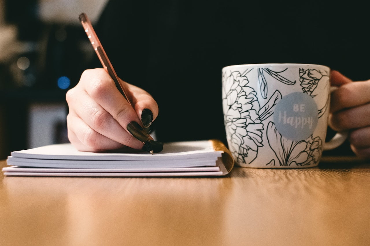 person holding a coffee mug and writing in journal