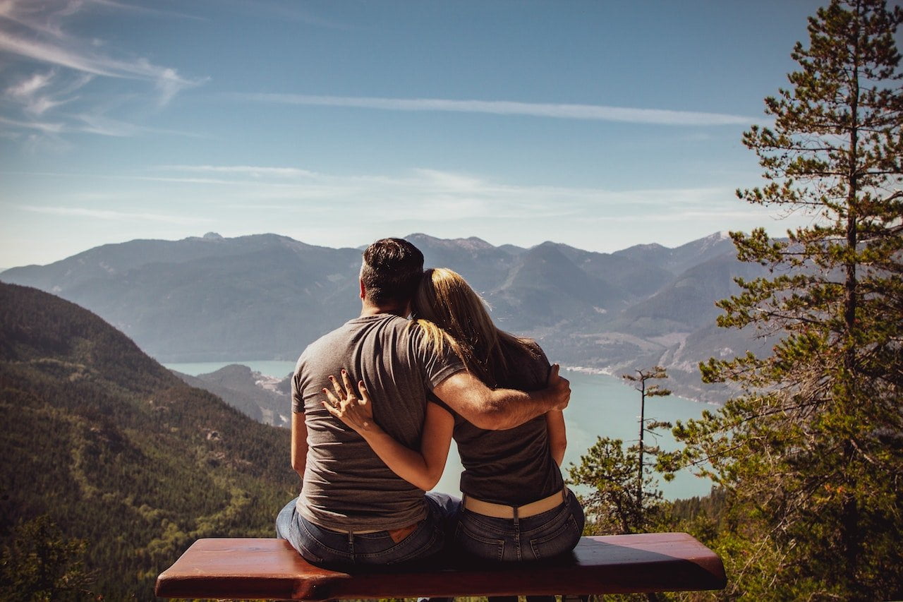 man and woman sitting on bench overlooking mountains