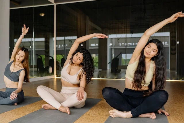 3 women sitting cross-legged doing an arm stretch