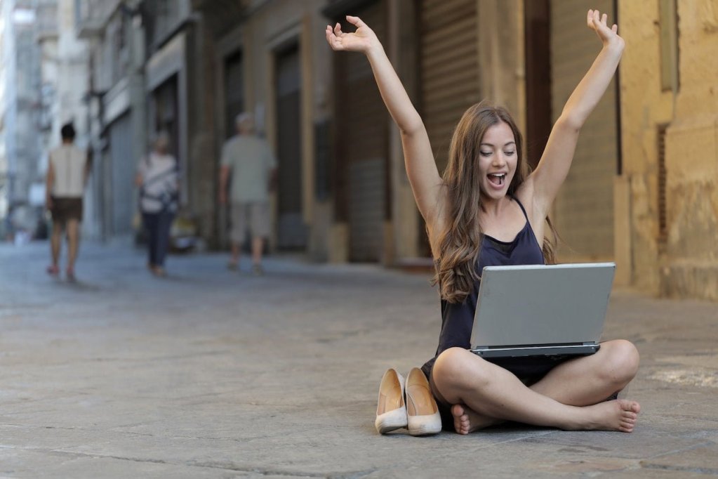 woman raising her hands while sitting on floor with laptop