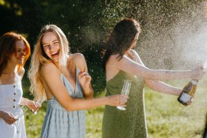 women laughing popping champagne cork.