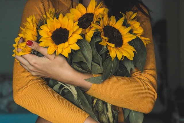 woman in yellow shirt holding fresh sunflowers