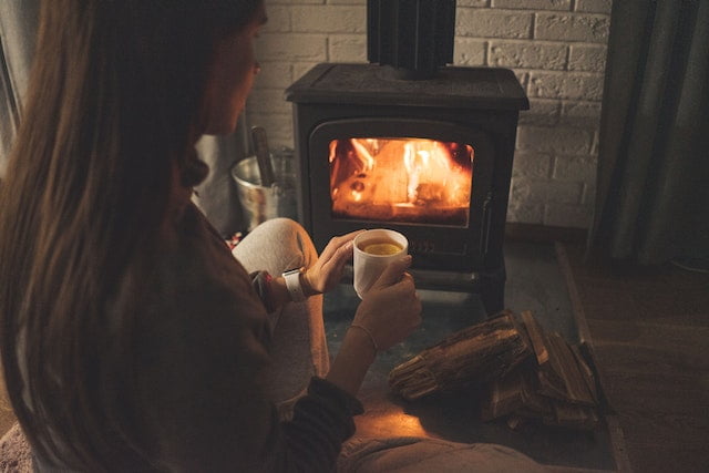 woman sitting in front of wood stove holding a cup of tea