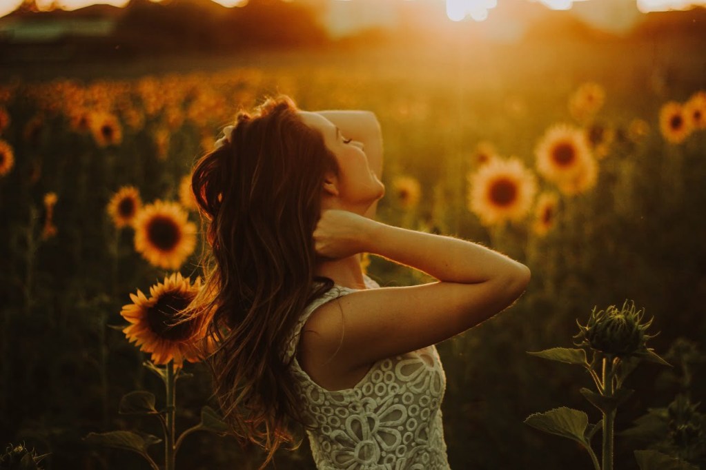 woman standing in sunflower field at sunset