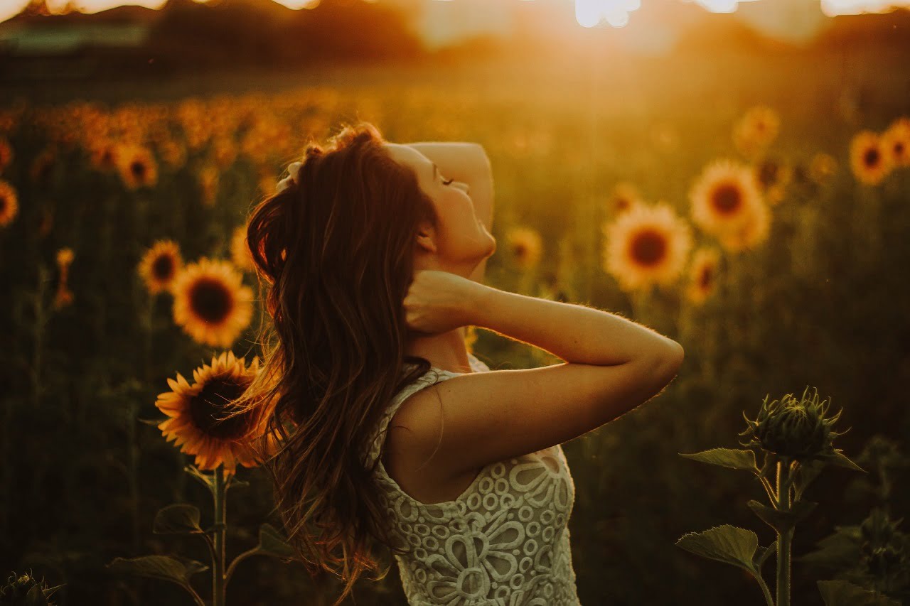 woman standing in sunflower field at sunset