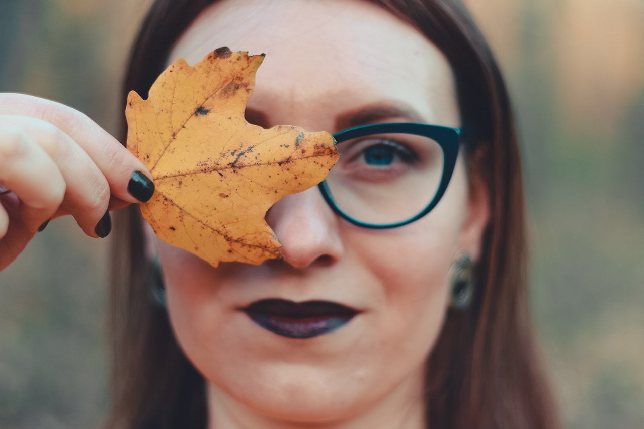Woman covering her face with autumn leaf