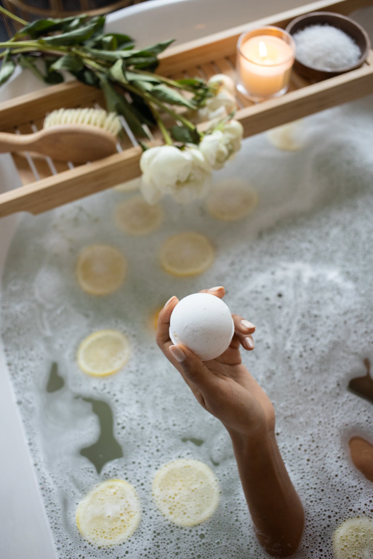 woman holding bath bomb in tub in front of bath tray  