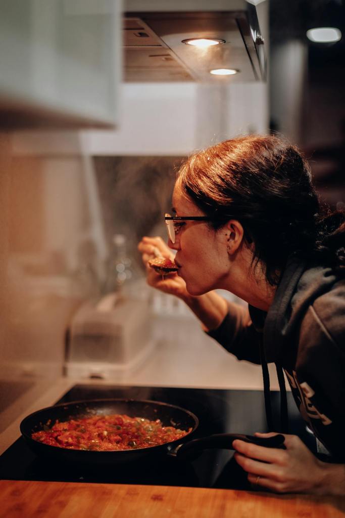 woman tasting food in pan on stove