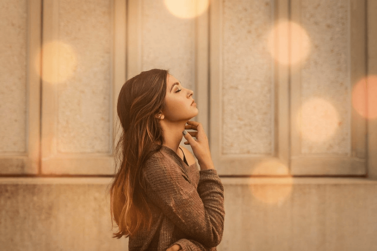 woman in brown shirt standing by wall with eyes closed